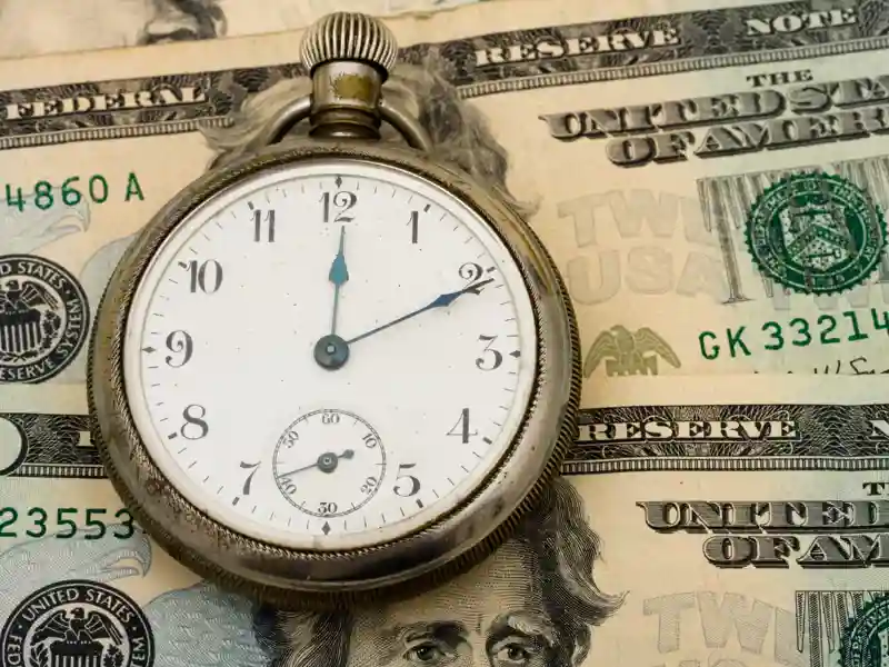 A pocket watch sitting on a twenty dollar bill background.