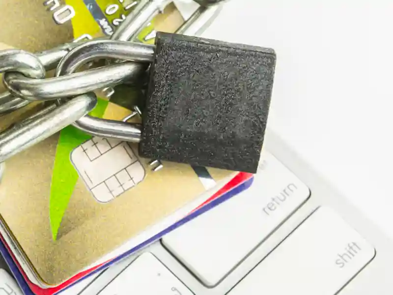 A padlock in a chain positioned on top of a keyboard and credit cards.