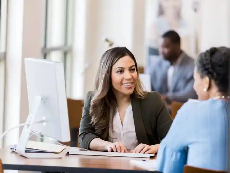 Bank manager smiles at customer as she types in information.