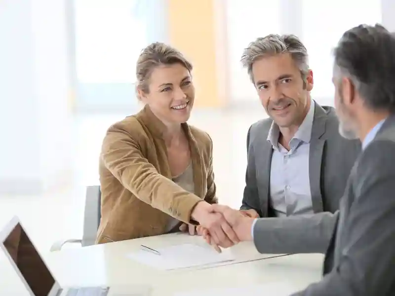 Couple in bank office shaking hand to financial advisor.