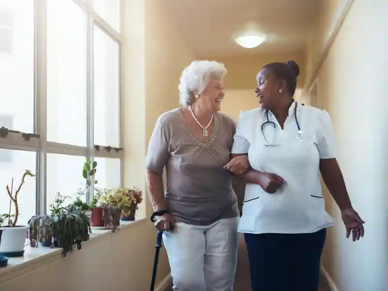 Happy elder woman gets help from nurse for a walk through the nursing home.