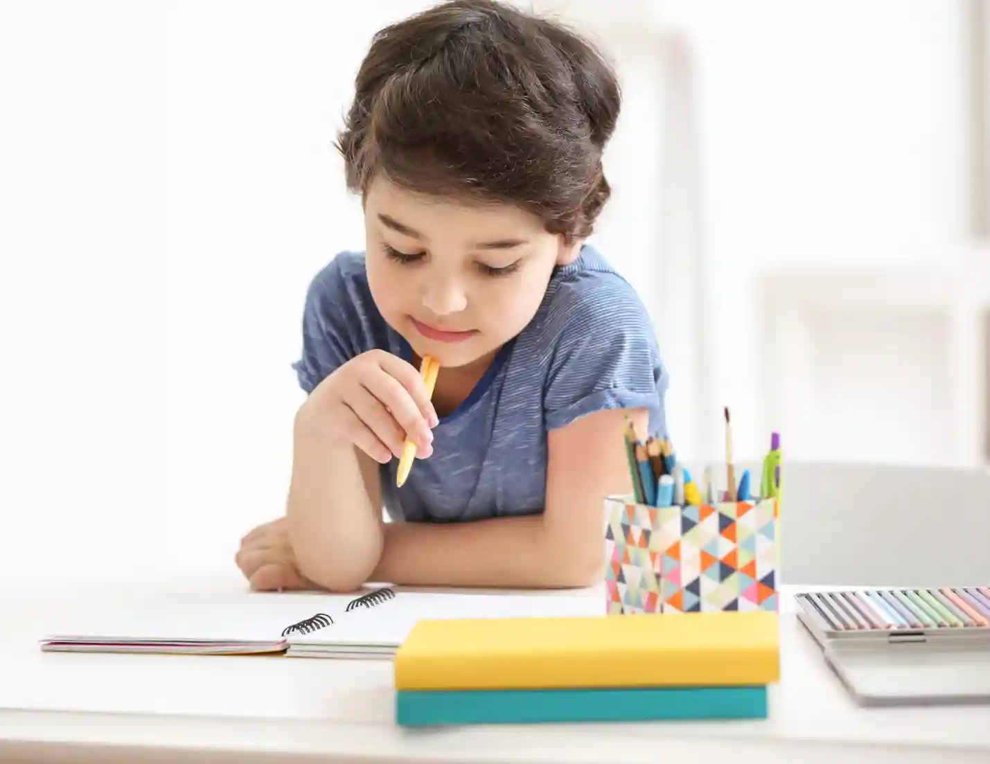 Child holding a pencil and looking at a notebook.
