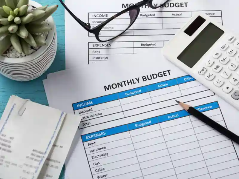 Calculator, pencil and receipts sitting on a monthly budget spreadsheet.