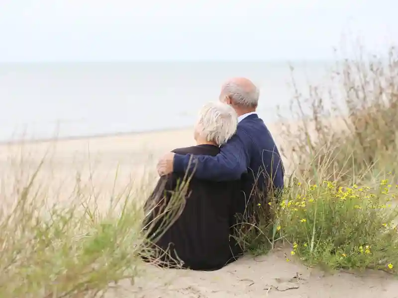 Man with his wife sitting together on sandy peaceful beach relaxing and looking at the ocean.