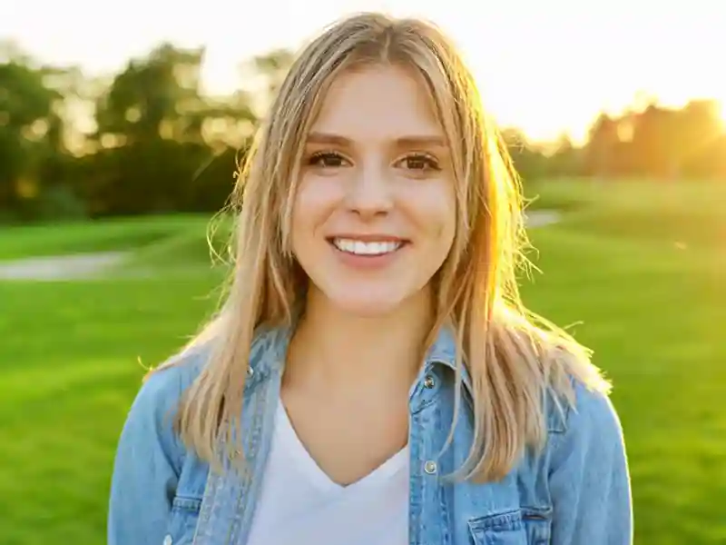 A girl smiling wide with greenery in the background