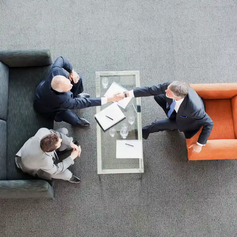 Businessmen shaking hands across coffee table in office lobby