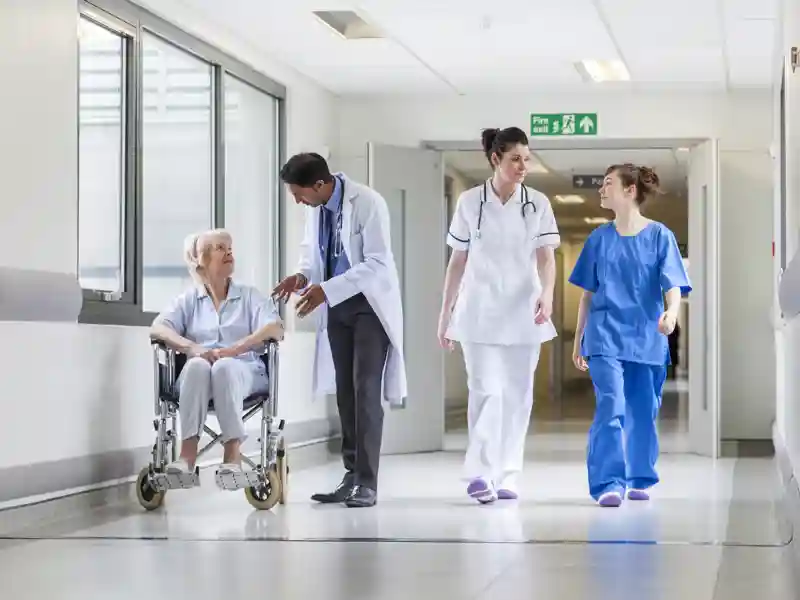Doctors and nurse in hospital corridor with senior female patient in wheelchair.