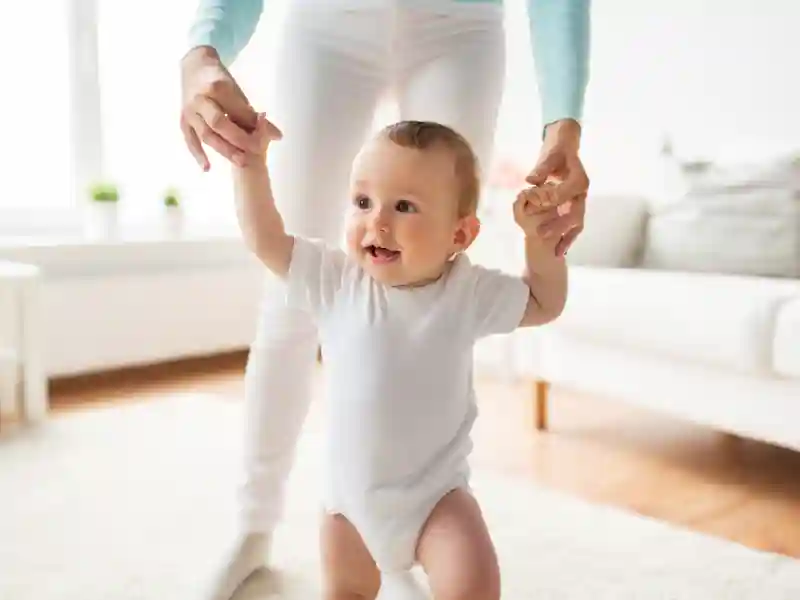 Happy little baby learning to walk with mother help at home.