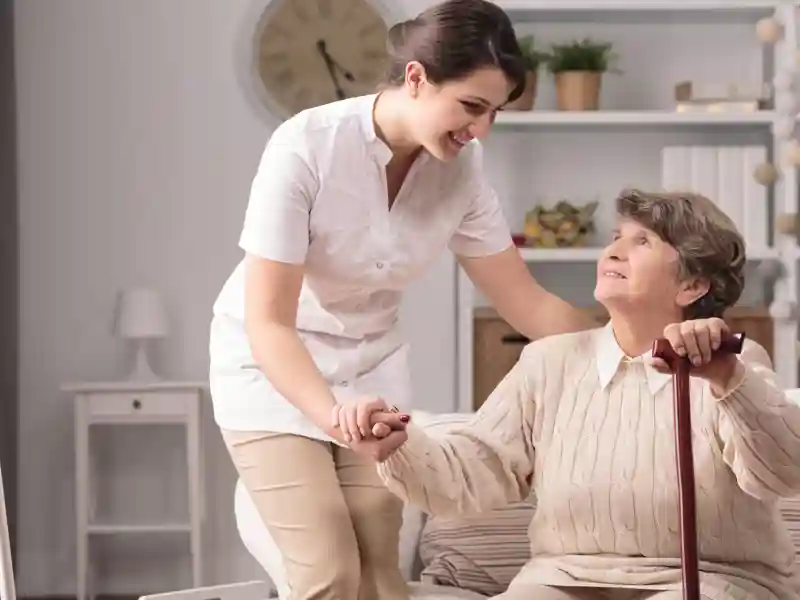 Young carer supporting senior disabled woman with walking stick.